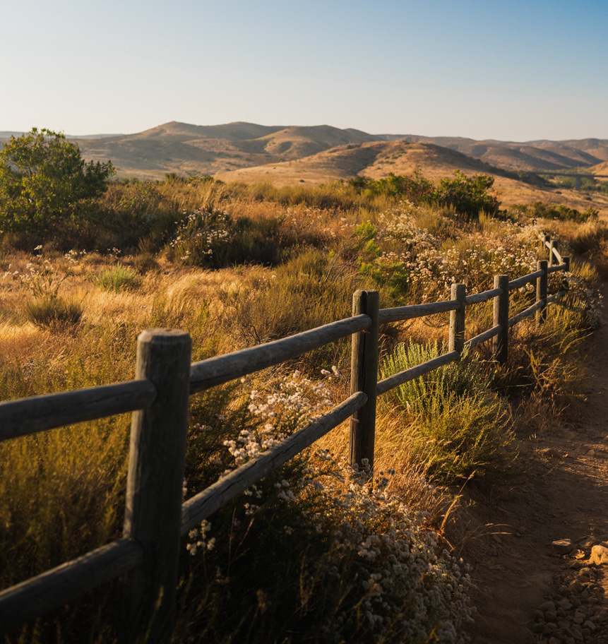 A wooden fence beside a sunlit trail and golden hills