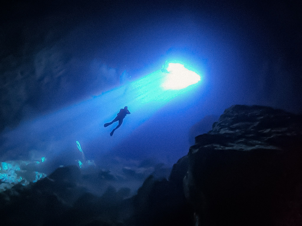 A diver silhouetted in a deep blue cavern beneath a bright opening
