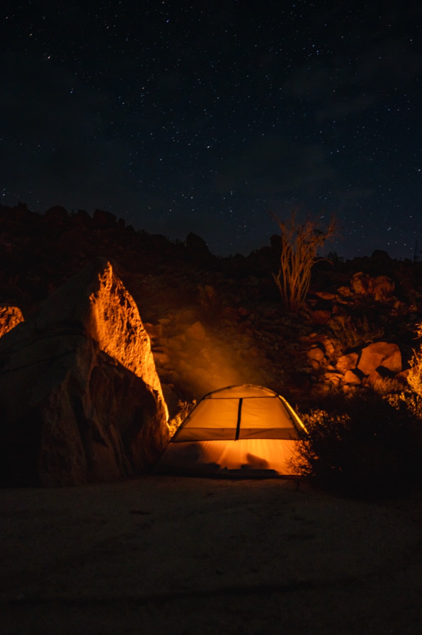 A glowing tent among desert rocks beneath stars