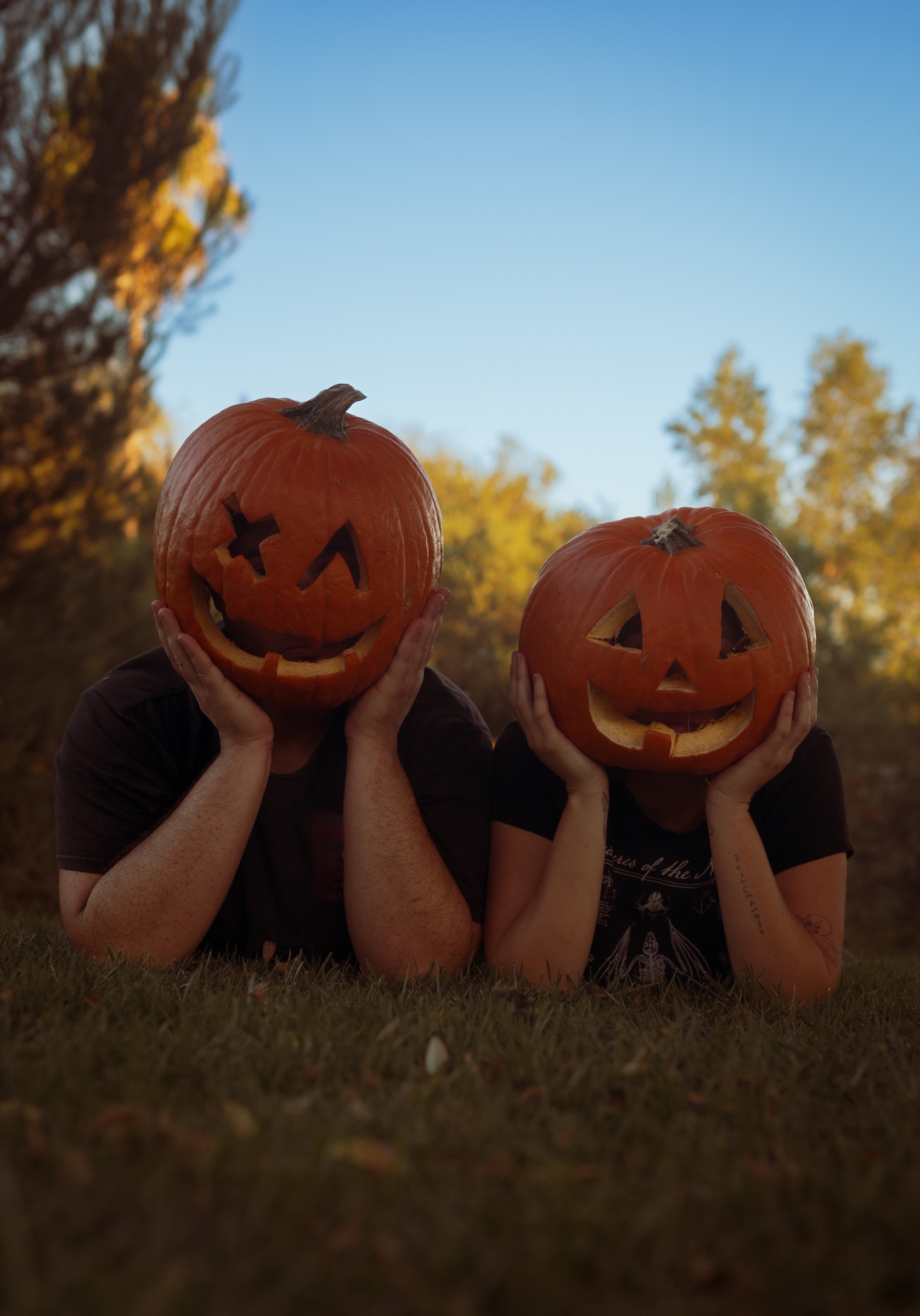 Two people lying on grass with carved pumpkins covering their faces