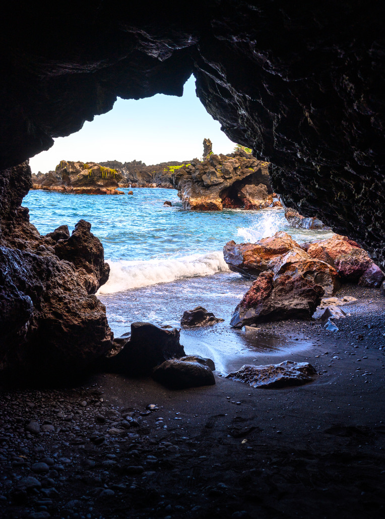 Blue surf and rocks seen through a dark sea cave opening