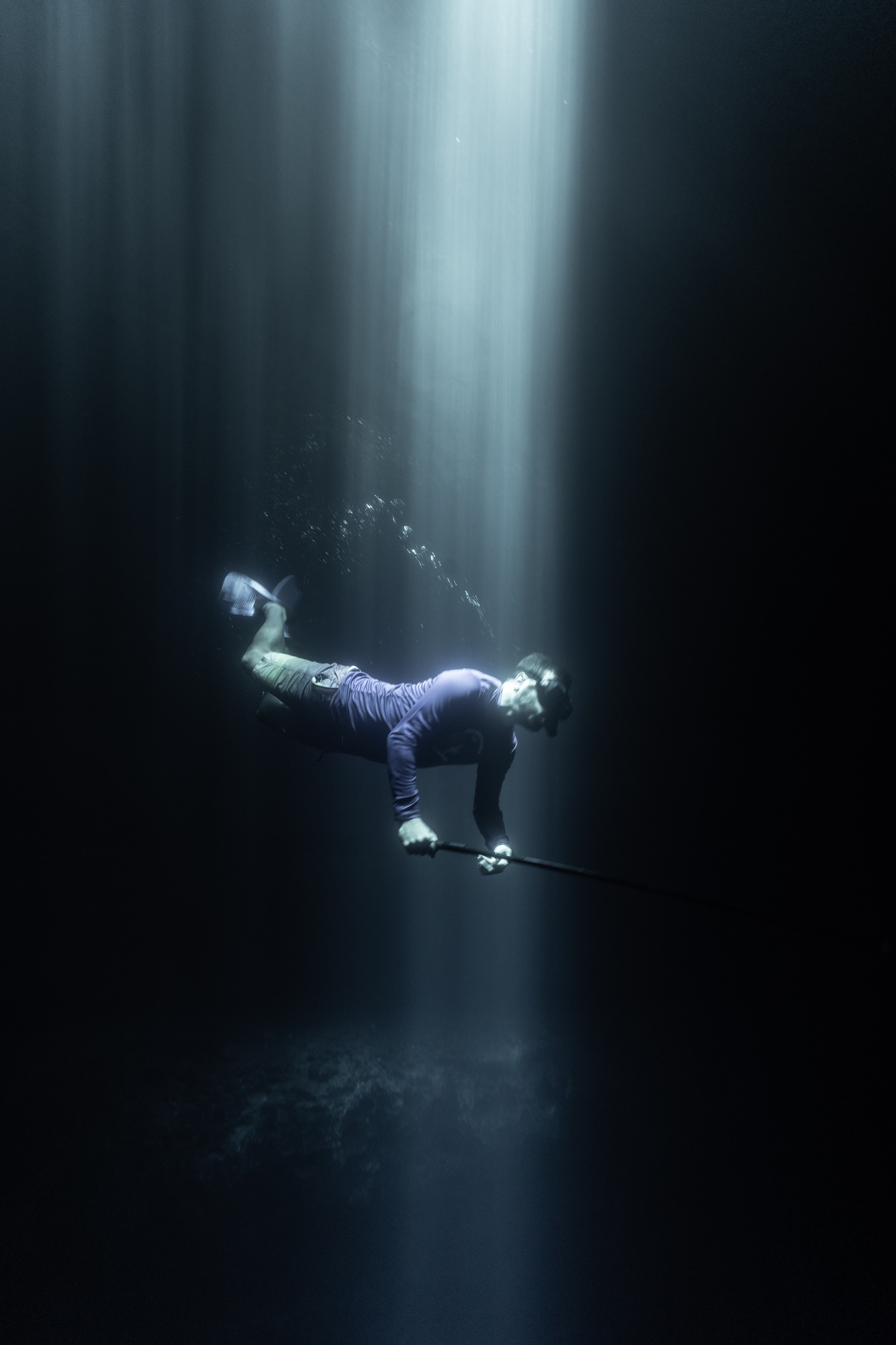 A diver suspended beneath a shaft of light in dark water