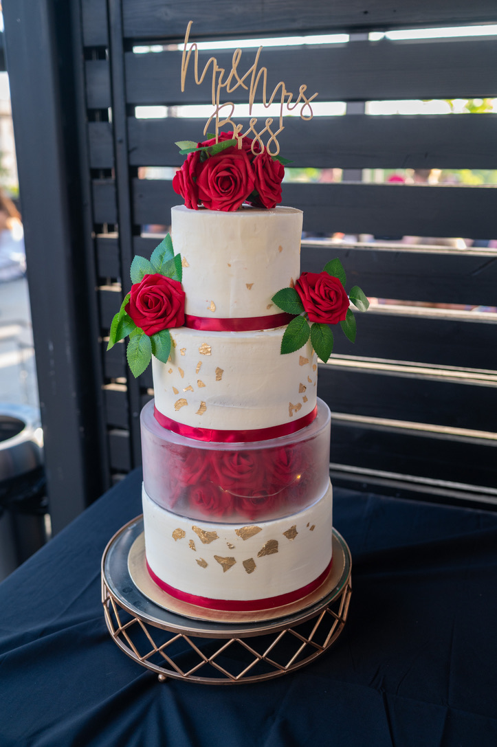 A tiered wedding cake decorated with red roses and gold leaf